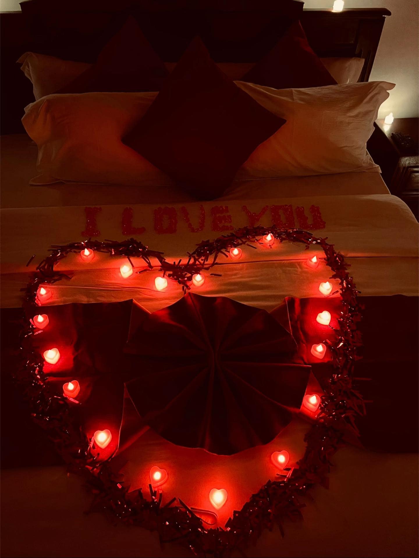 Détail du lit — « I LOVE YOU » en lettres rouges, grand cœur de bougies LED et serviette pliée en éventail