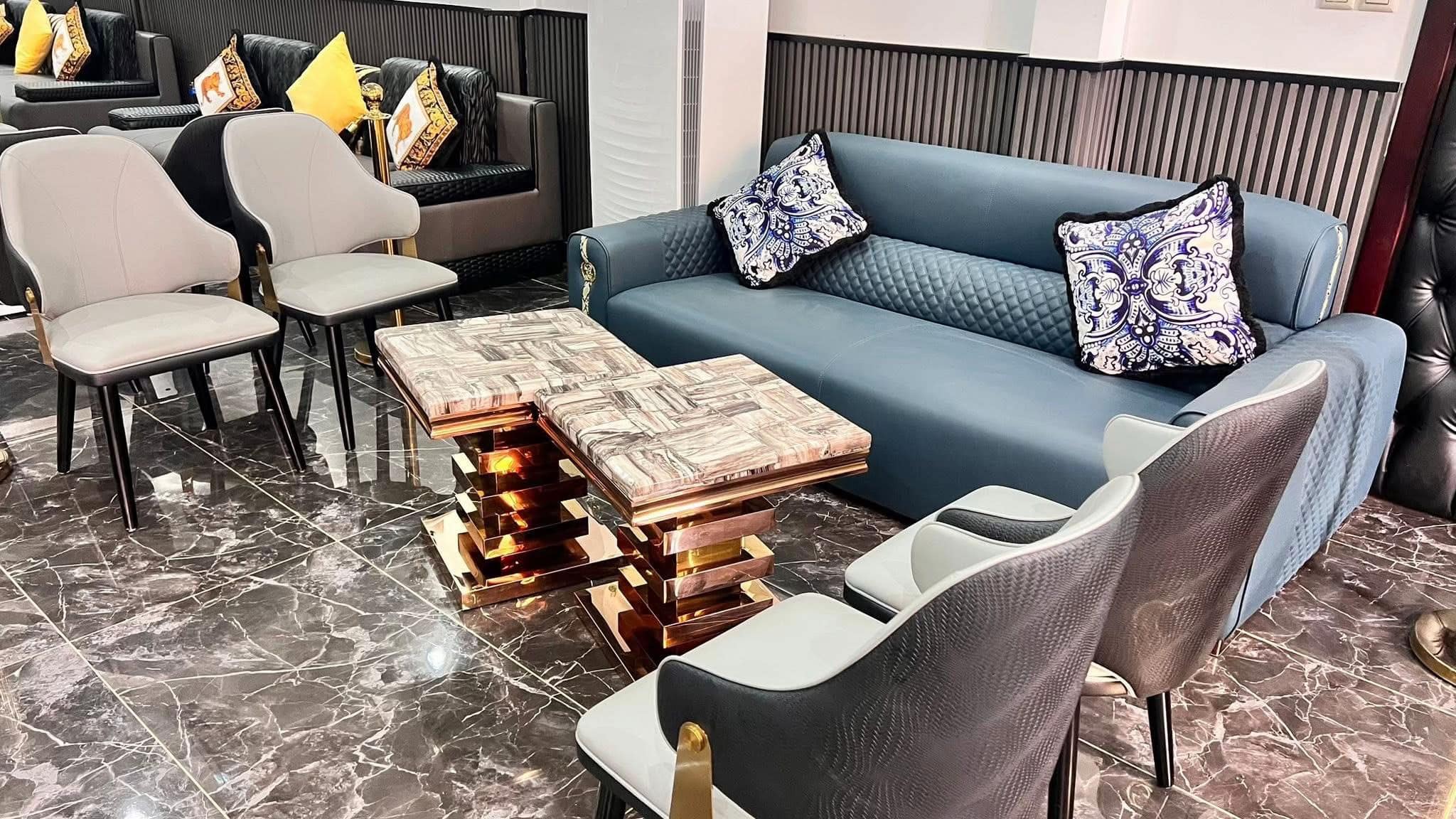 Canapé bleu matelassé, coussins baroques et tables en marbre sur socle cuivré