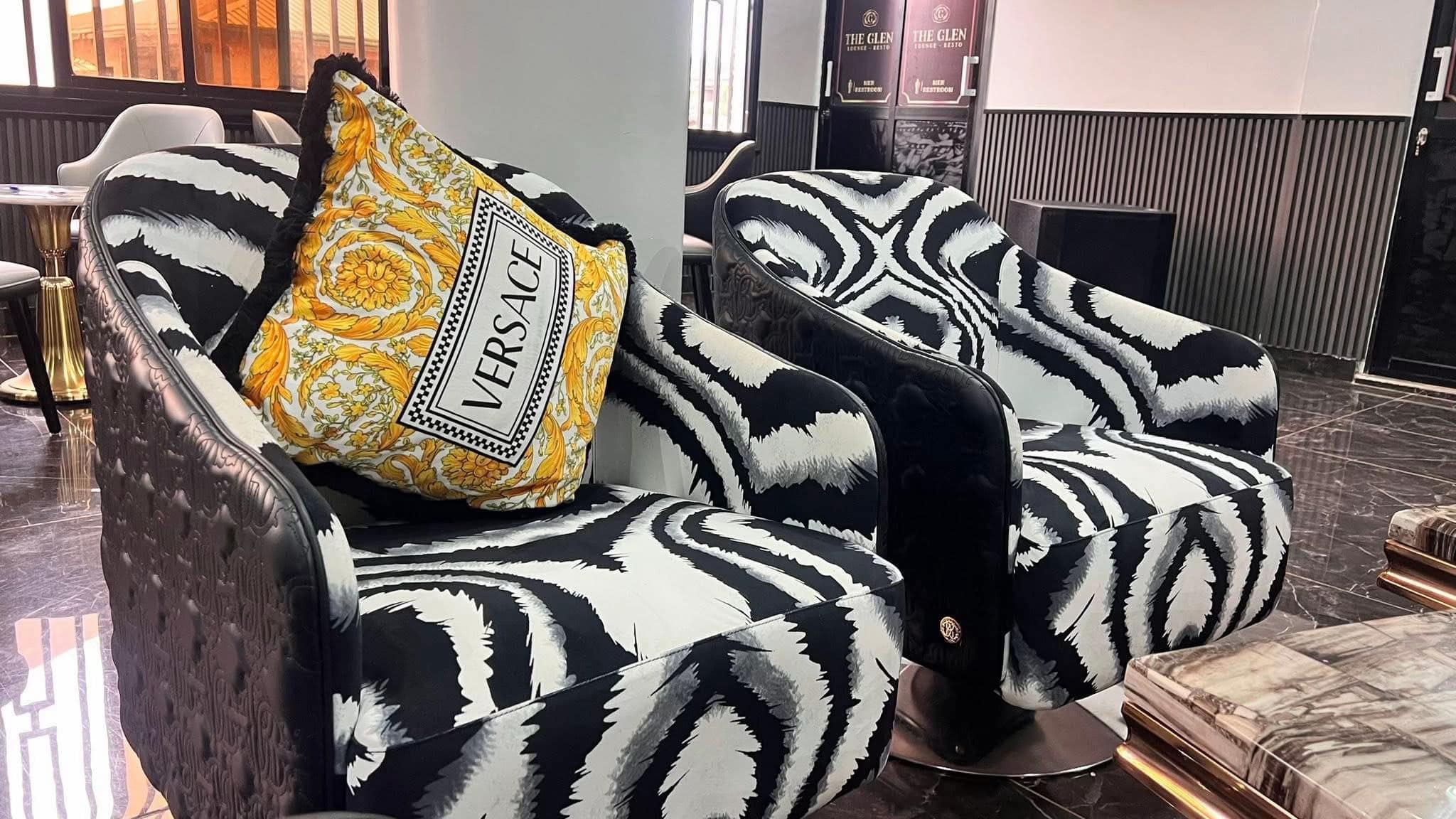 Détail — fauteuils zébrés et coussin Versace, enseigne « The Glen · Lounge-Resto » au fond