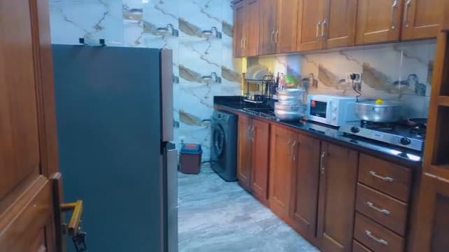 Cuisine de l’appartement A10 — grand réfrigérateur-congélateur, meubles en bois verni, plan de travail en granit noir, plaque gaz, micro-ondes, égouttoir garni et crédence en marbre