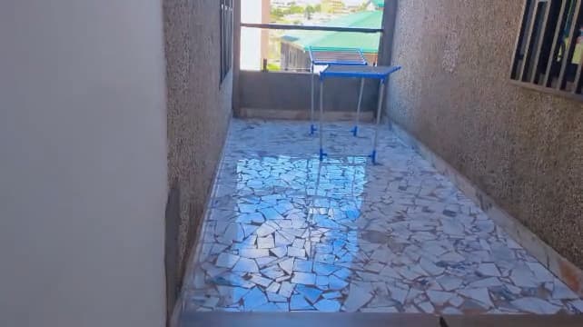 Terrasse de service de l’appartement A10 — sol en opus de marbre, murs crépis, garde-corps métallique, étendoir pliant et vue sur les toits voisins