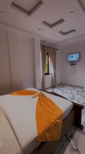 Chambre de l’appartement A10 — le lit, la télévision murale et la fenêtre à rideaux, sol en marbre
