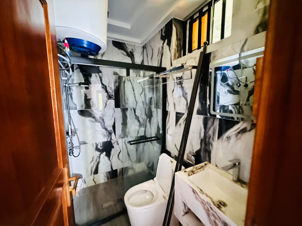 Deuxième salle de douche de l’appartement A40 — chauffe-eau électrique mural, marbre noir et blanc, douchette sur barre, WC, plan vasque en marbre et imposte vitrée