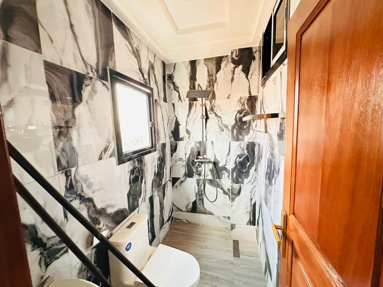Troisième salle de douche de l’appartement A40 — marbre noir et blanc, colonne de douche avec ciel de pluie et douchette sur barre, mitigeur thermostatique, WC, miroir encadré et petite fenêtre