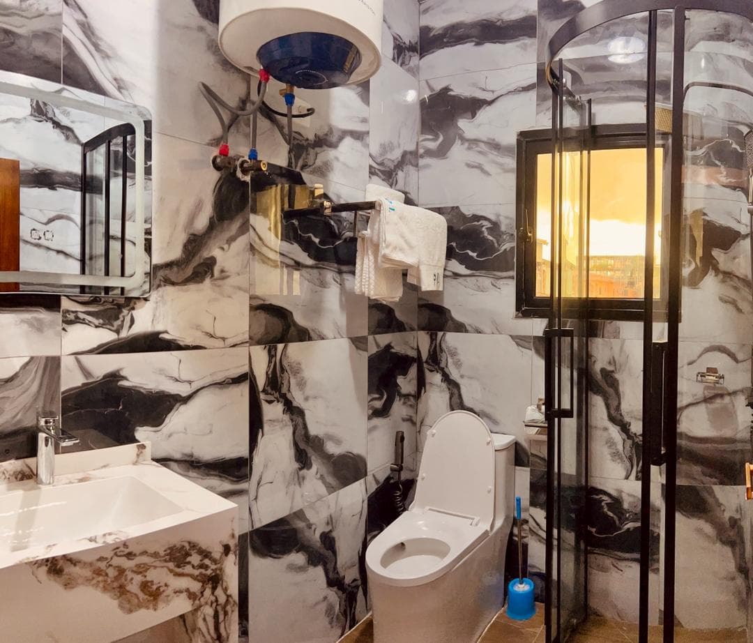 Seconde douche du studio SS101 — cabine de douche d’angle vitrée, vasque, miroir et chauffe-eau