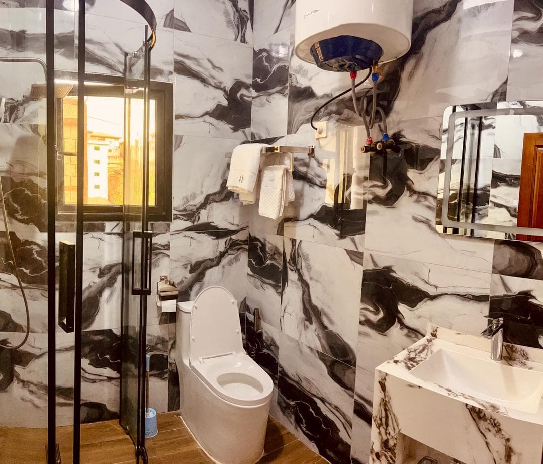Douche du studio SS140 — faïence marbrée noir et blanc, cabine de douche vitrée à profilés noirs, vasque en marbre, miroir, serviettes et chauffe-eau