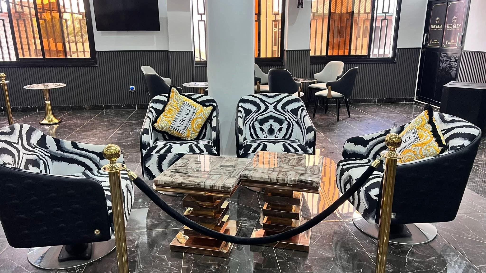 Salon du Glen Lounge — fauteuils zébrés, coussins Versace, poteaux dorés et cordon noir sur marbre poli